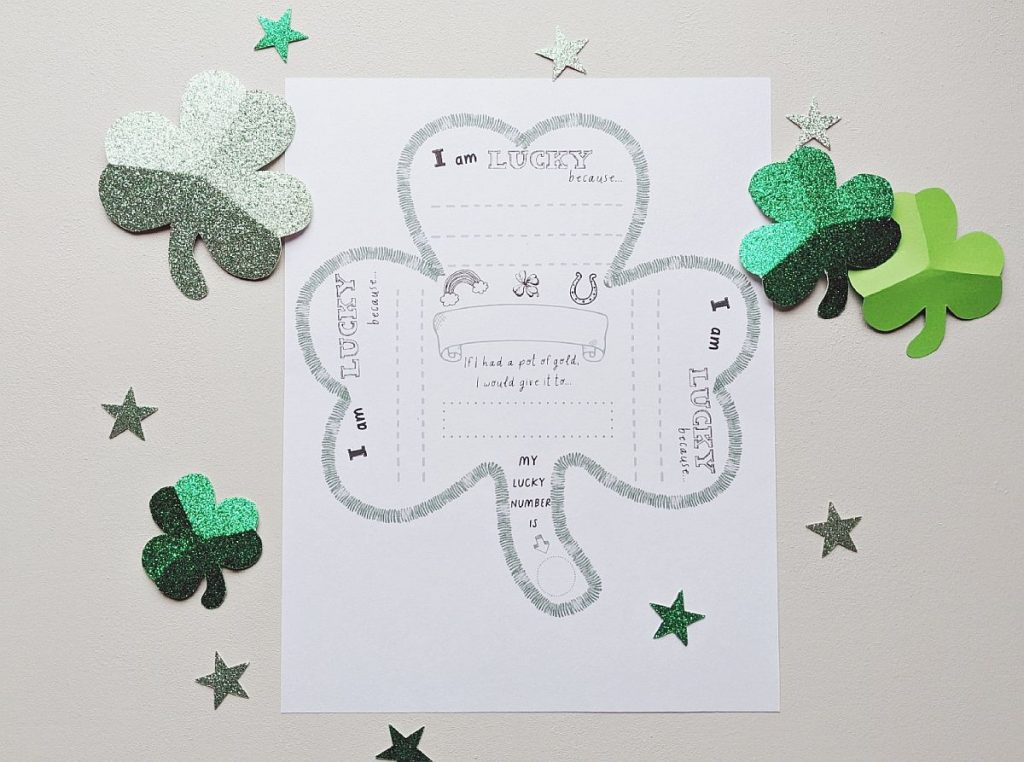 A St. Patrick's Day printable activity page for children. It features a shamrock image with the phrase I am lucky because and blank spaces to fill in. Surrounded by sparkly green cut out shamrocks.